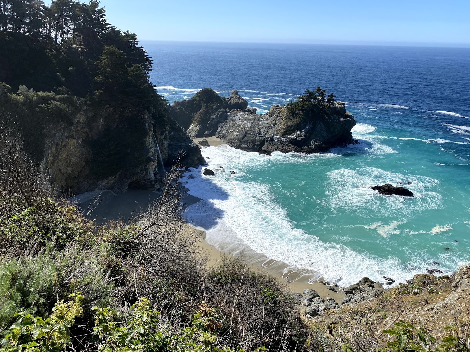 a beach with rocks and trees with McWay Falls in the background