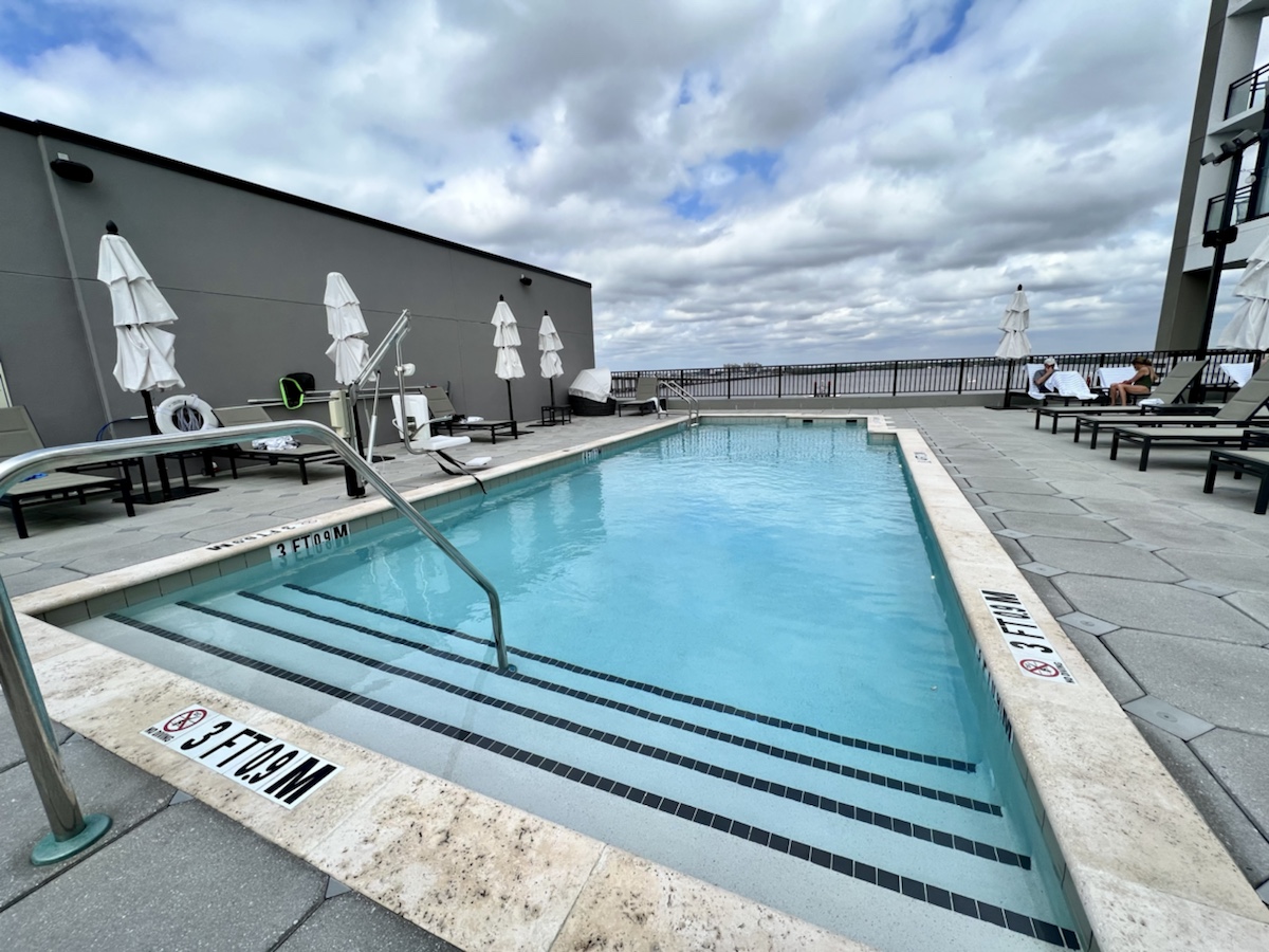 a pool with a railing and chairs on a rooftop