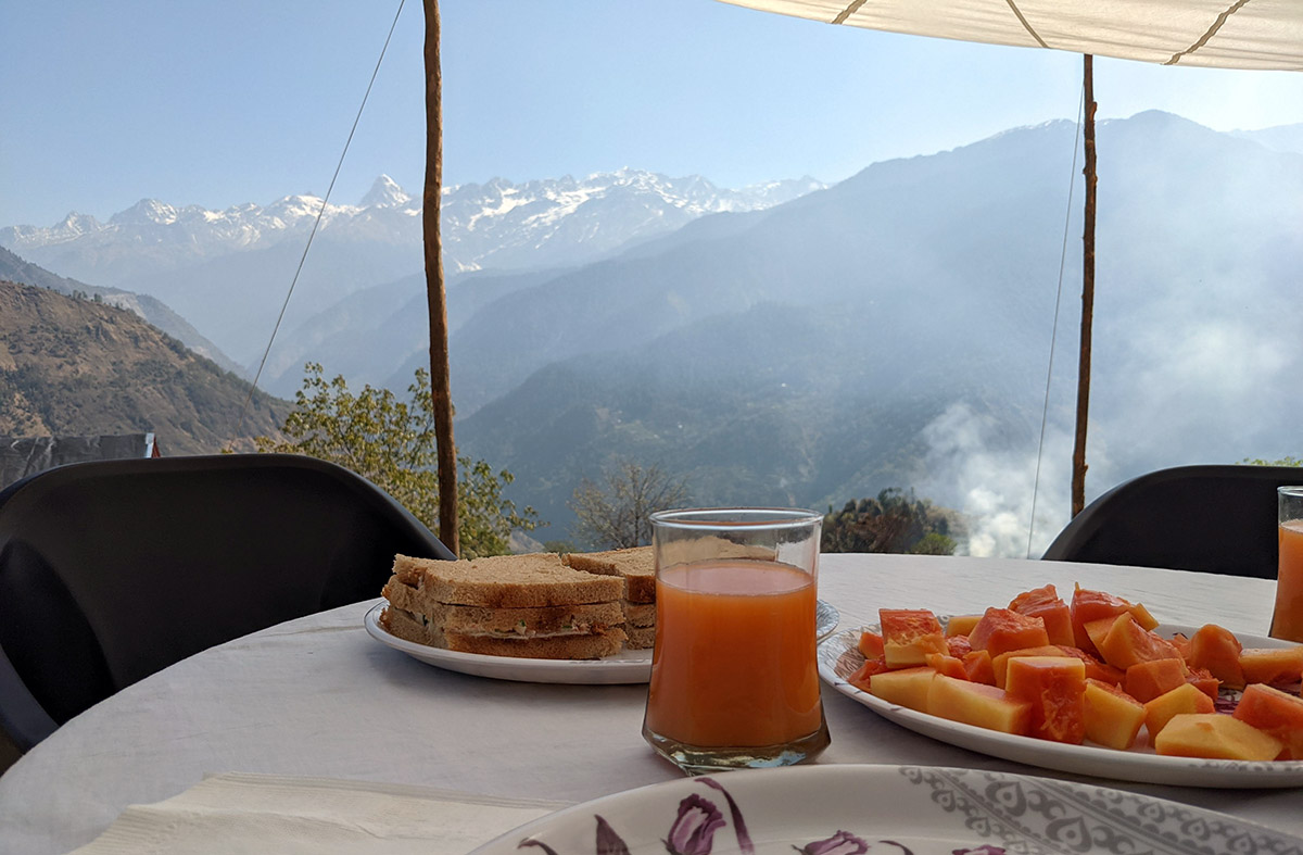 a plate of food and a glass of juice on a table with mountains in the background