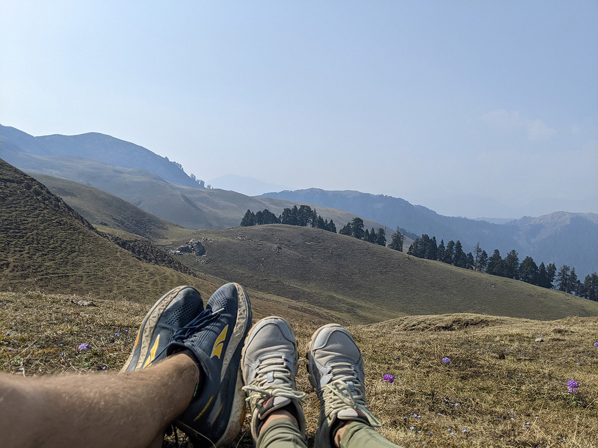 a pair of legs and feet in a grassy area with mountains in the background