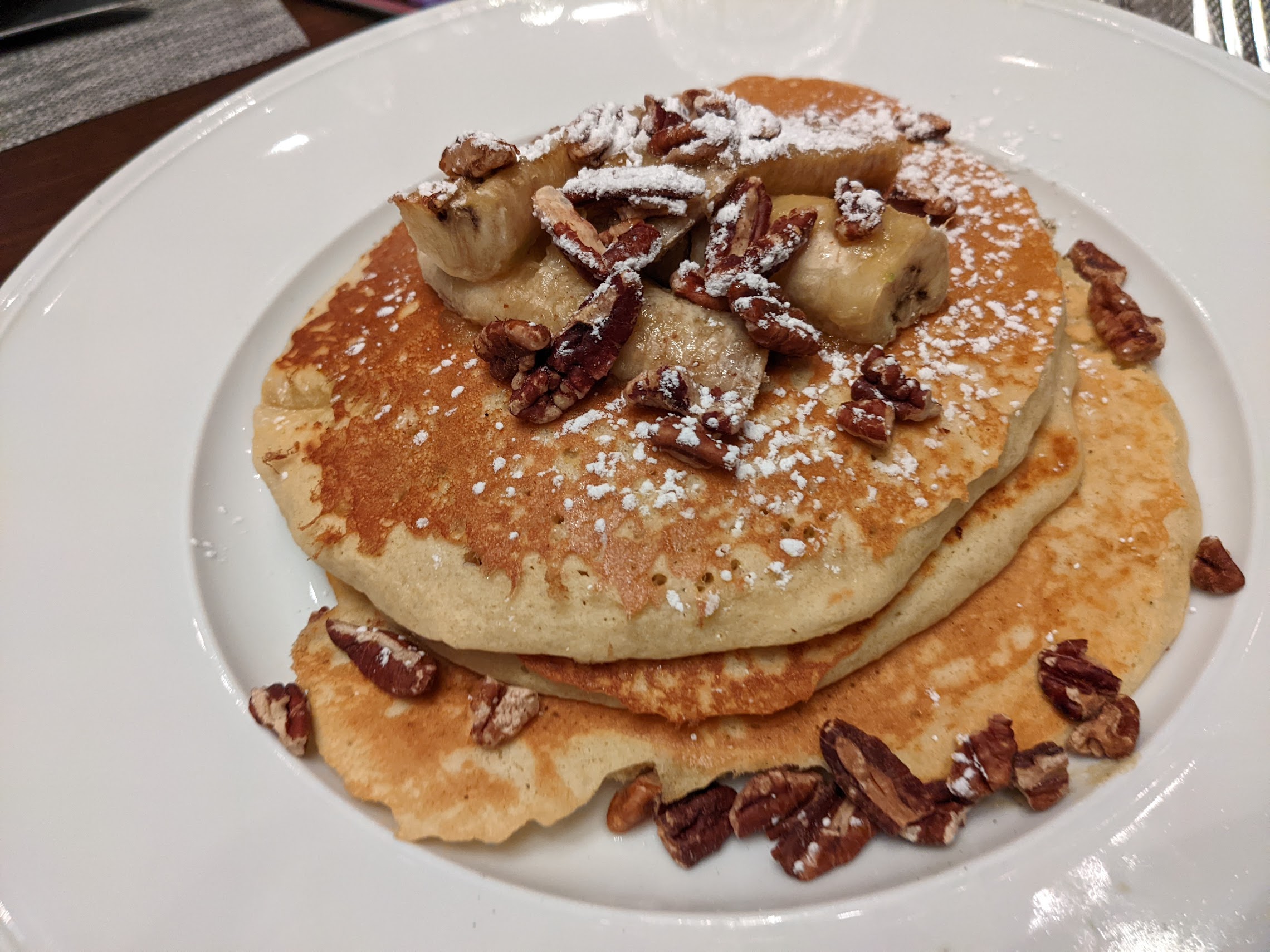 a stack of pancakes with bananas and pecans on top