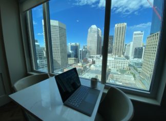 a laptop on a table with a cup and a window