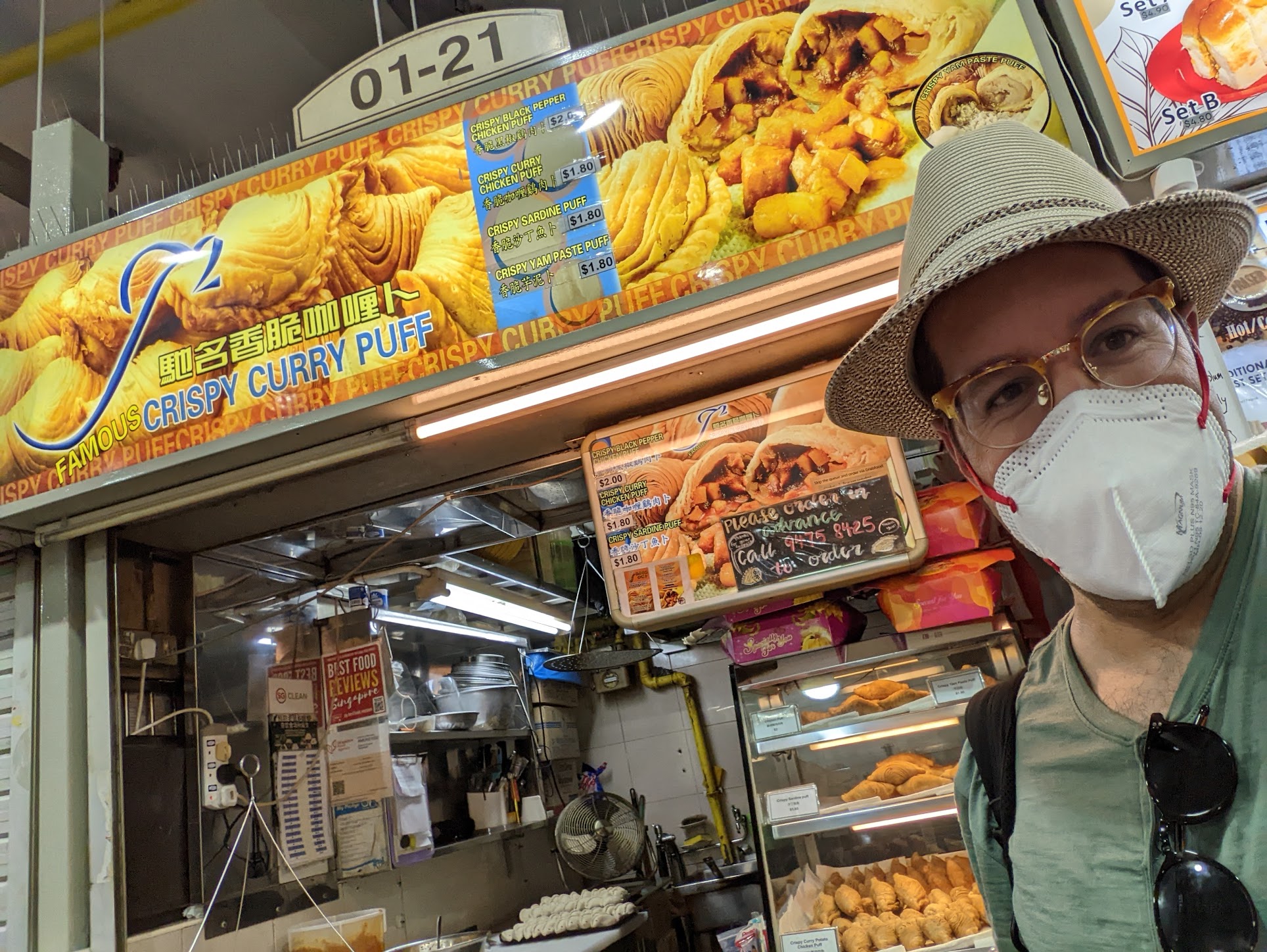a man wearing a face mask and a hat standing in front of a food stand