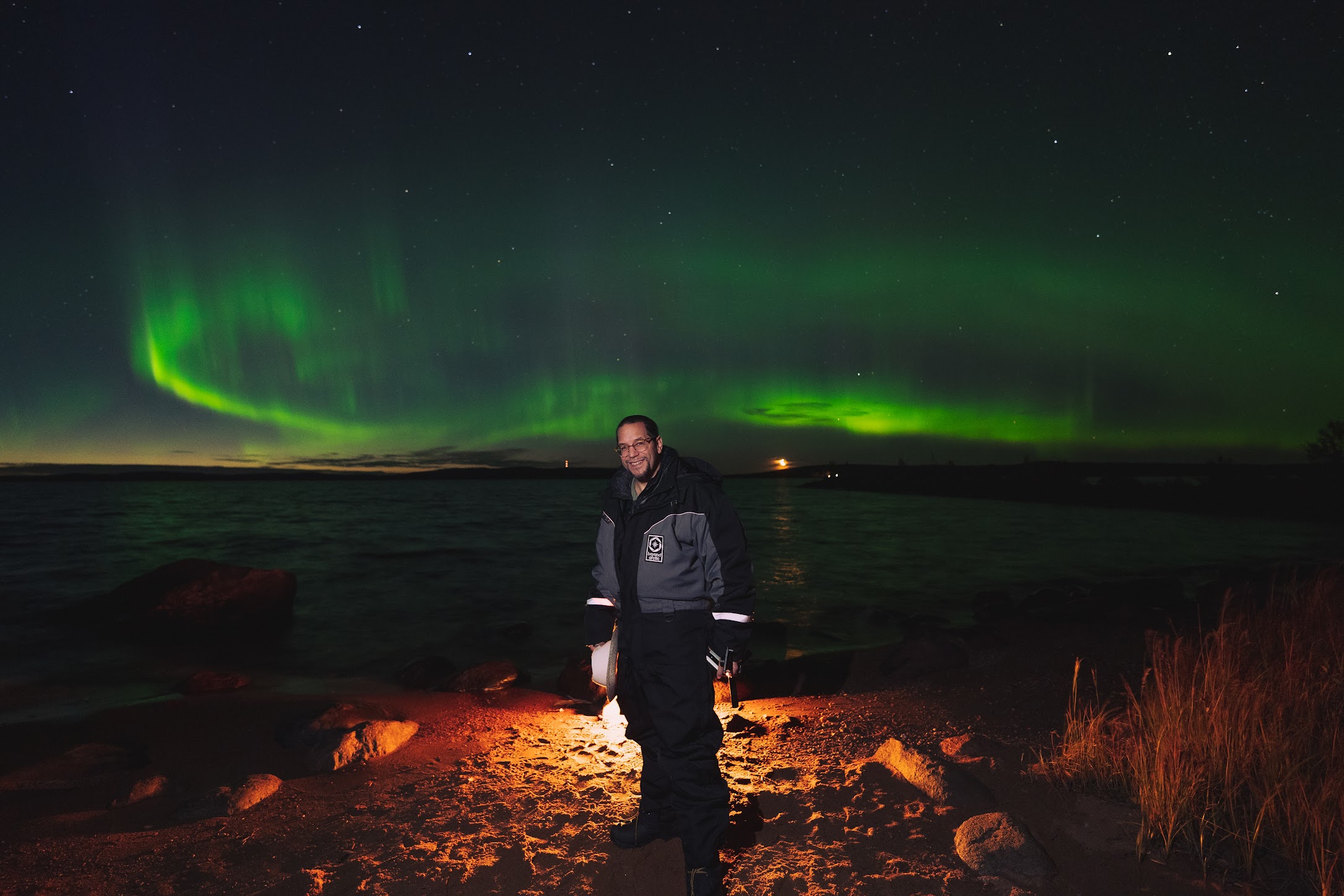 a man standing on a beach with a green aurora borealis in the background