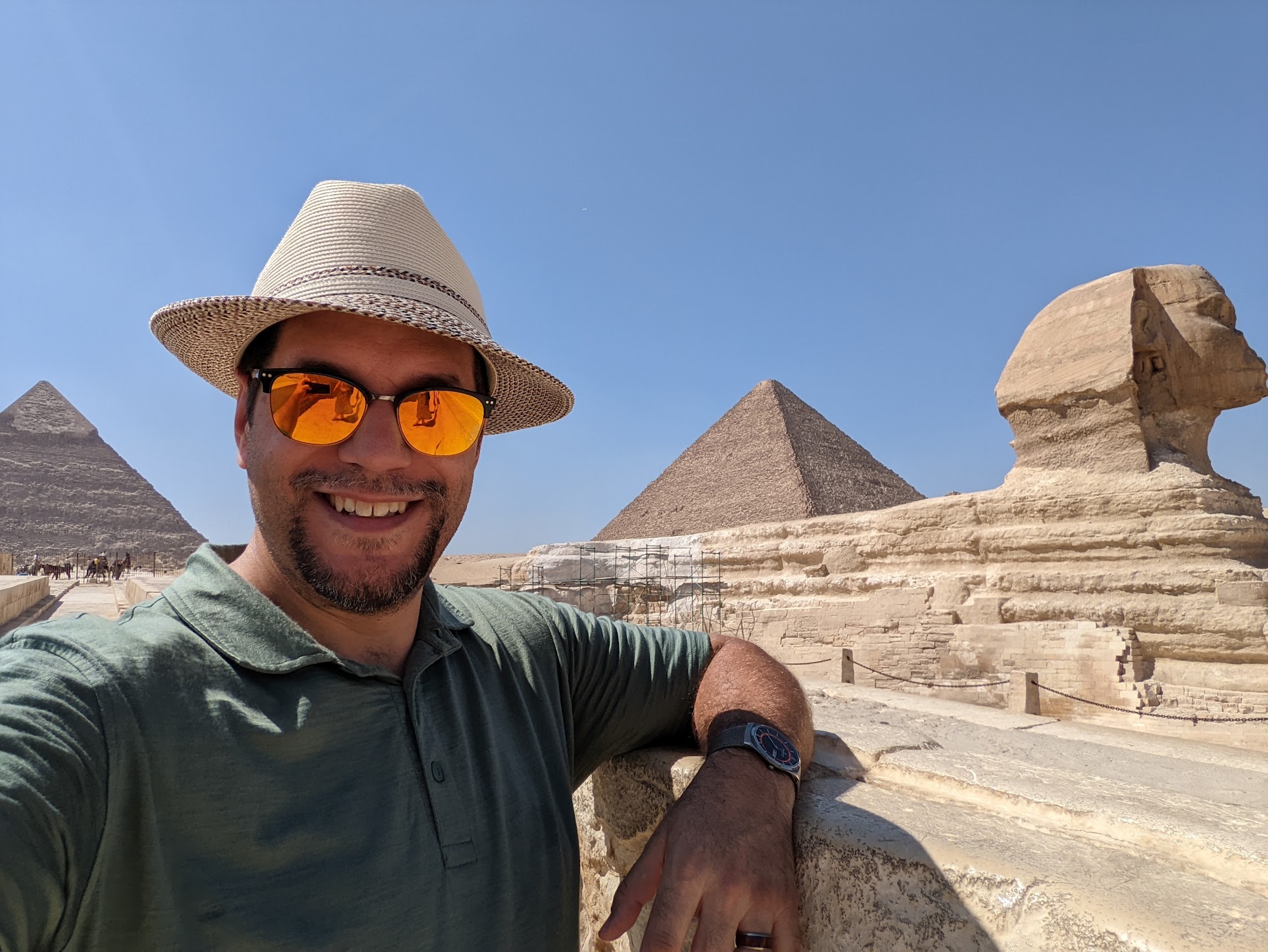 a man in a hat and sunglasses leaning on a stone ledge in front of pyramids