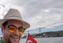 a man in a hat and sunglasses on a boat with a flag