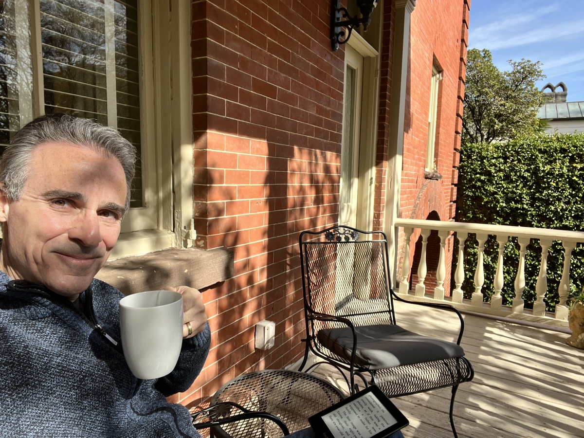 a man holding a cup and a tablet on a porch