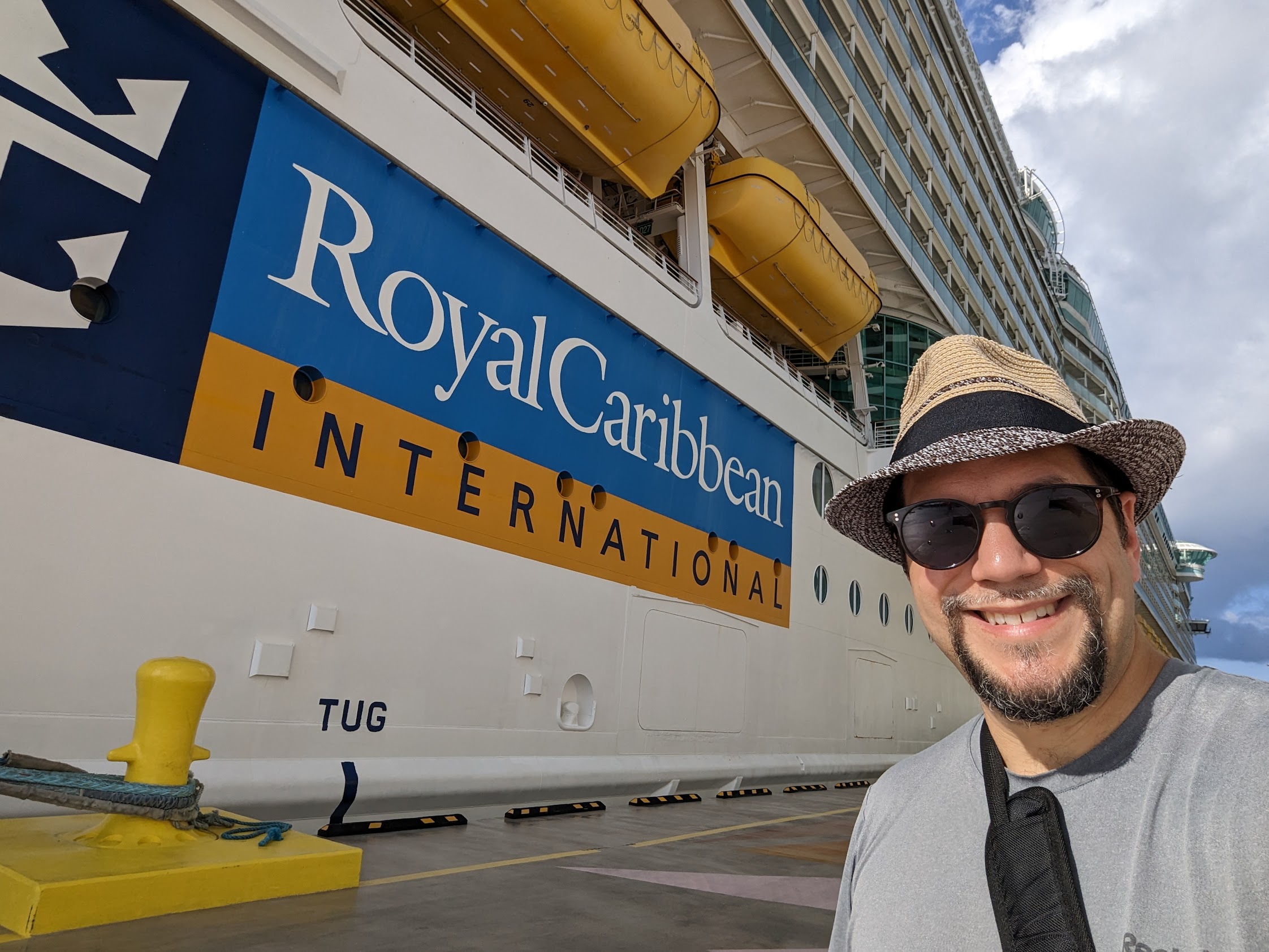 a man in a hat and sunglasses standing in front of a large cruise ship