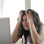 a woman holding her head in front of a laptop