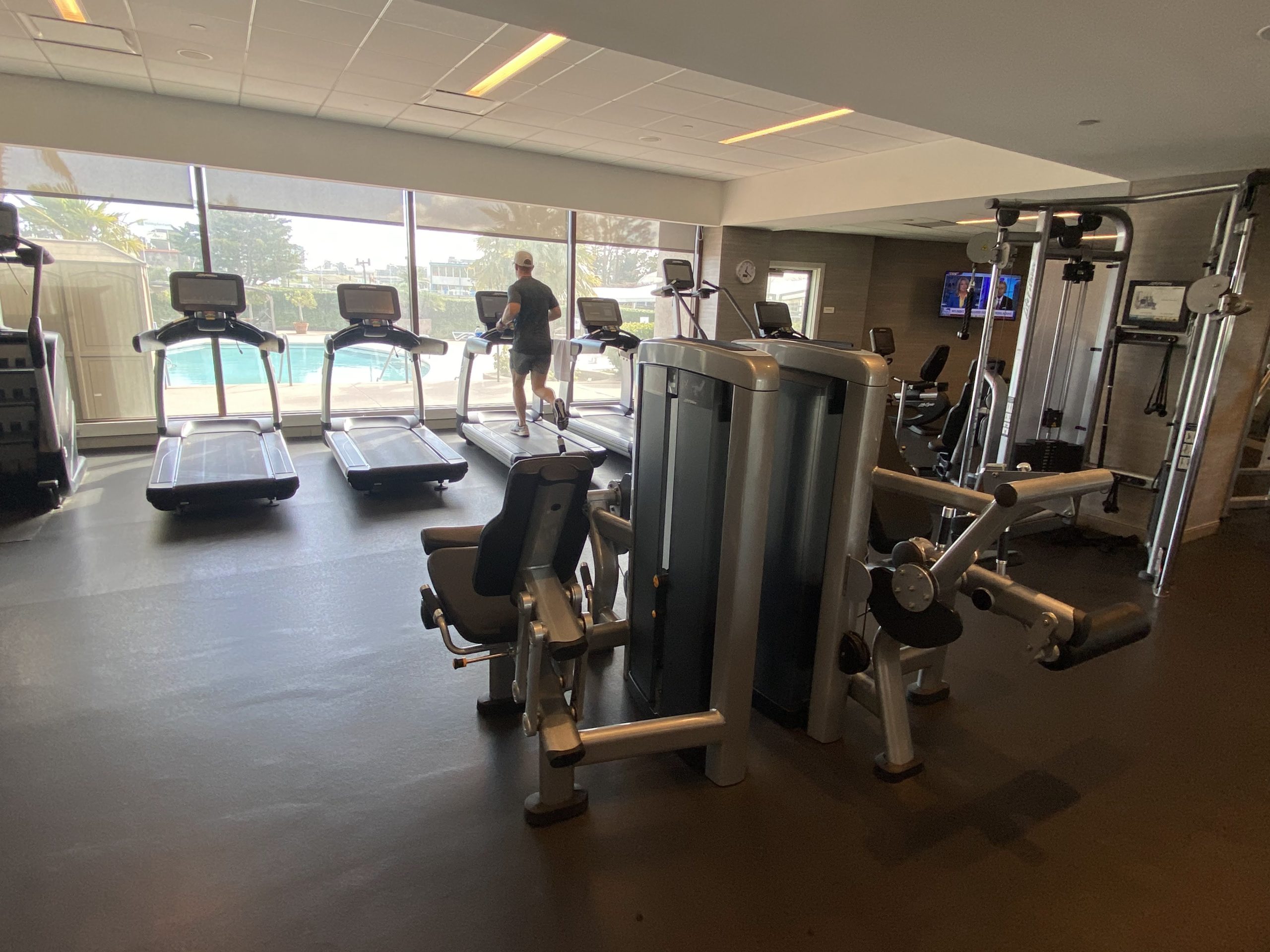 a gym with several treadmills and a man standing in the background