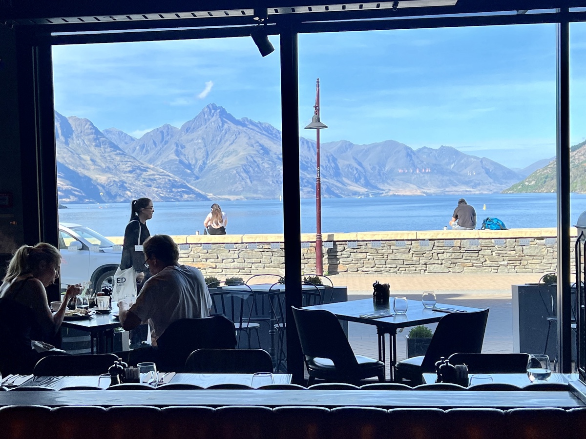a group of people sitting at tables outside a building with a view of mountains and water