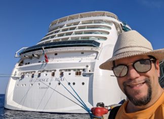 a man in a hat and sunglasses standing in front of a large cruise ship