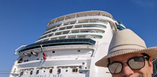a man in a hat and sunglasses standing in front of a large cruise ship