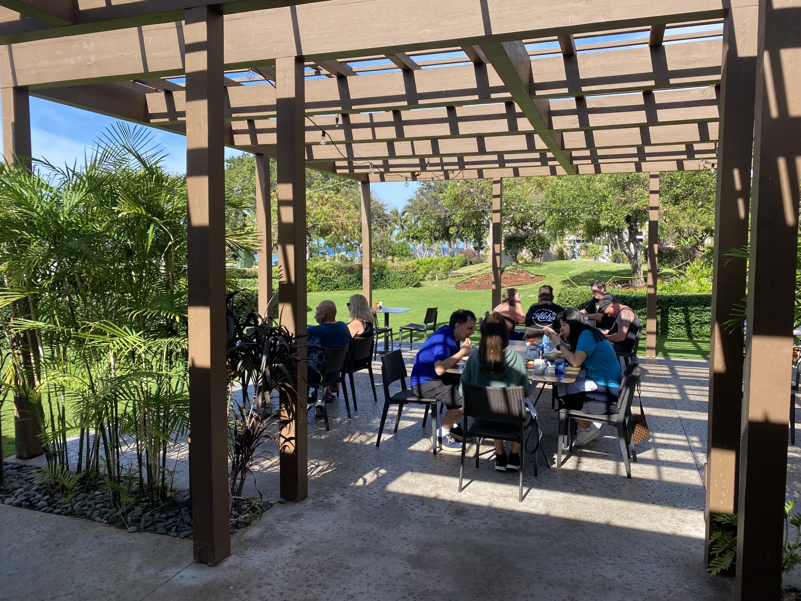 a group of people sitting at tables under a pergola