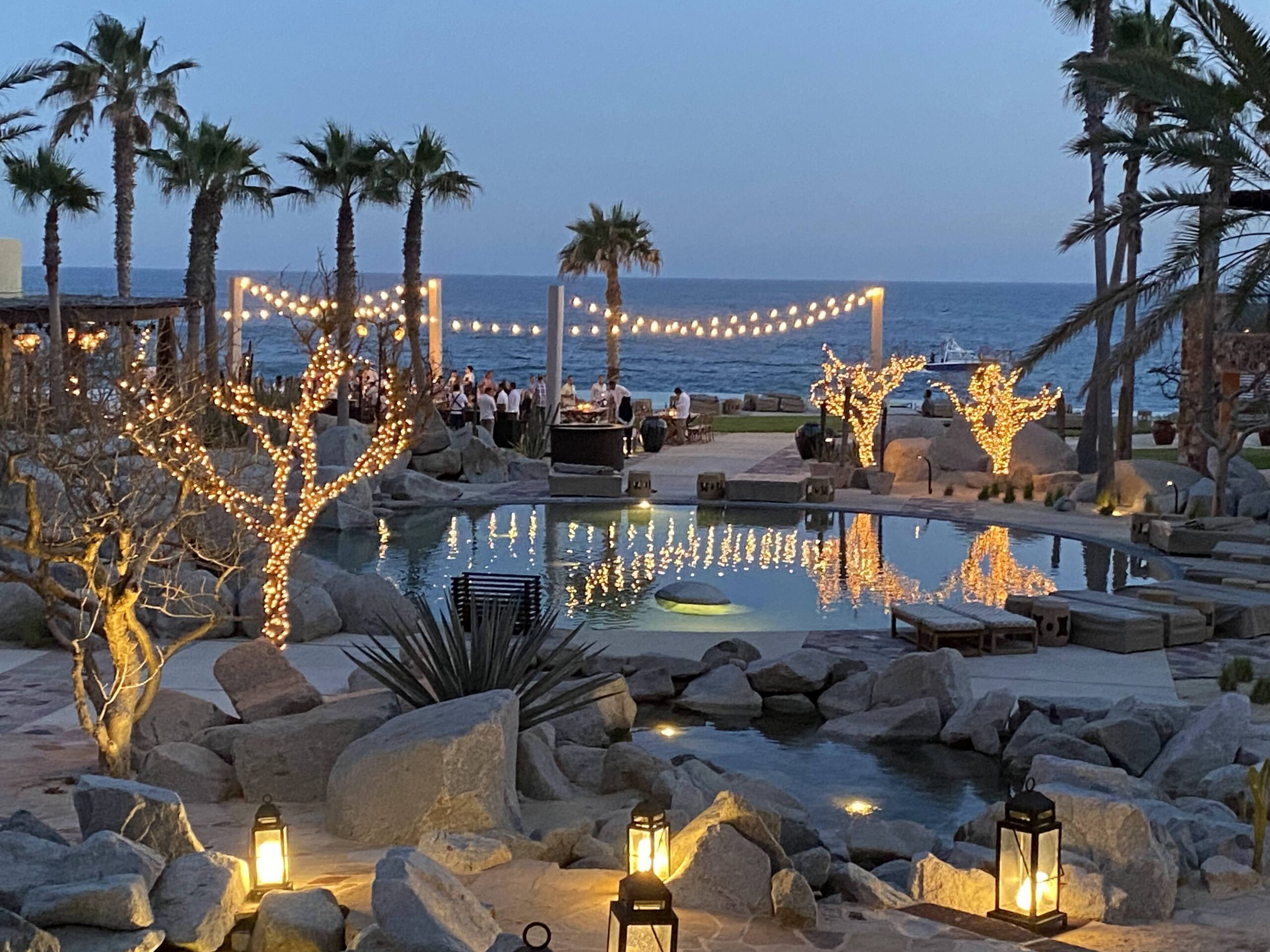a pool with lights and palm trees and people in the background