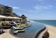 a pool with lounge chairs and umbrellas on the beach