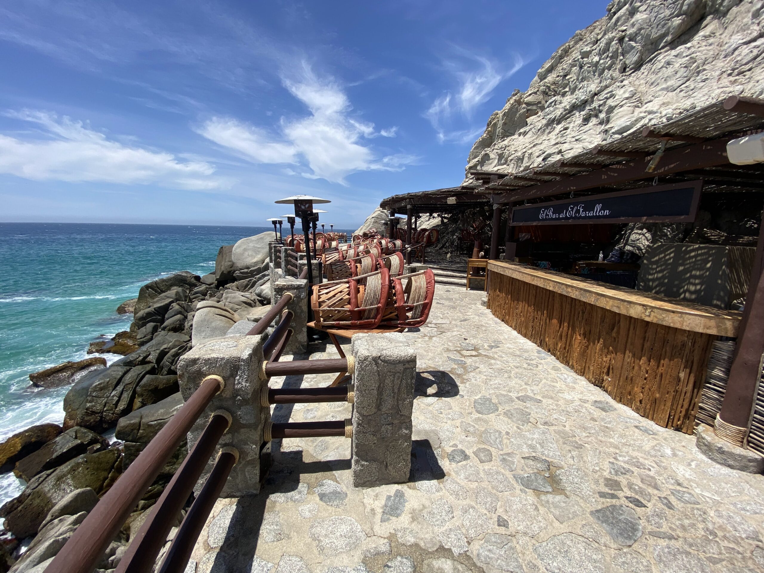 a stone walkway with a bar and chairs on the side of a cliff