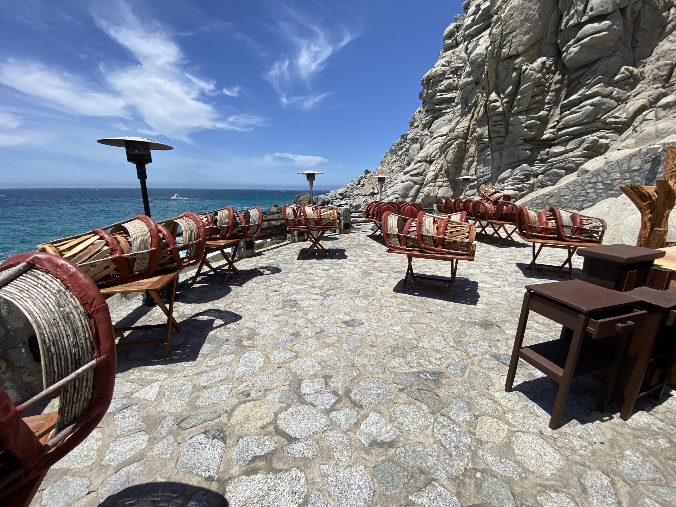 chairs on a stone patio with a cliff and water in the background