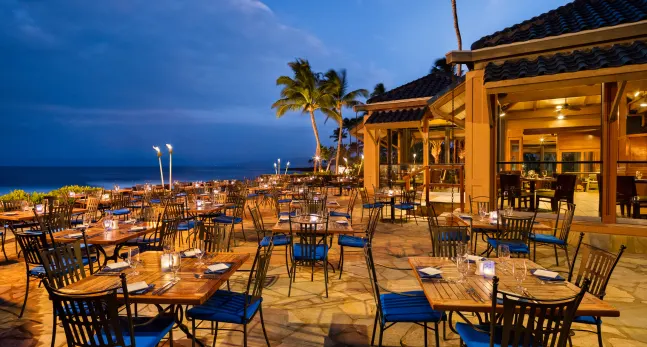 tables outside a restaurant with palm trees and a blue sky