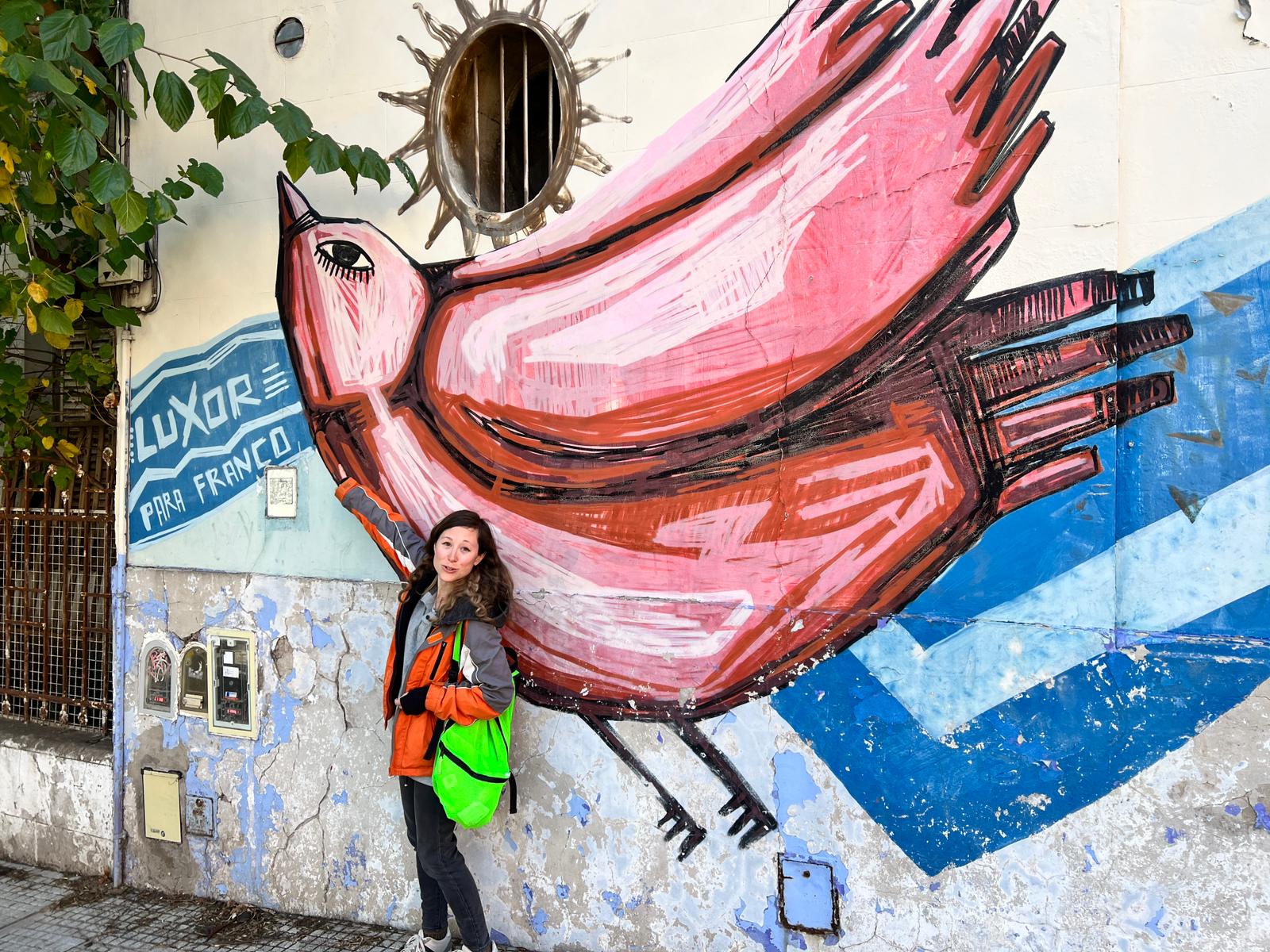 a woman standing next to a mural of a bird