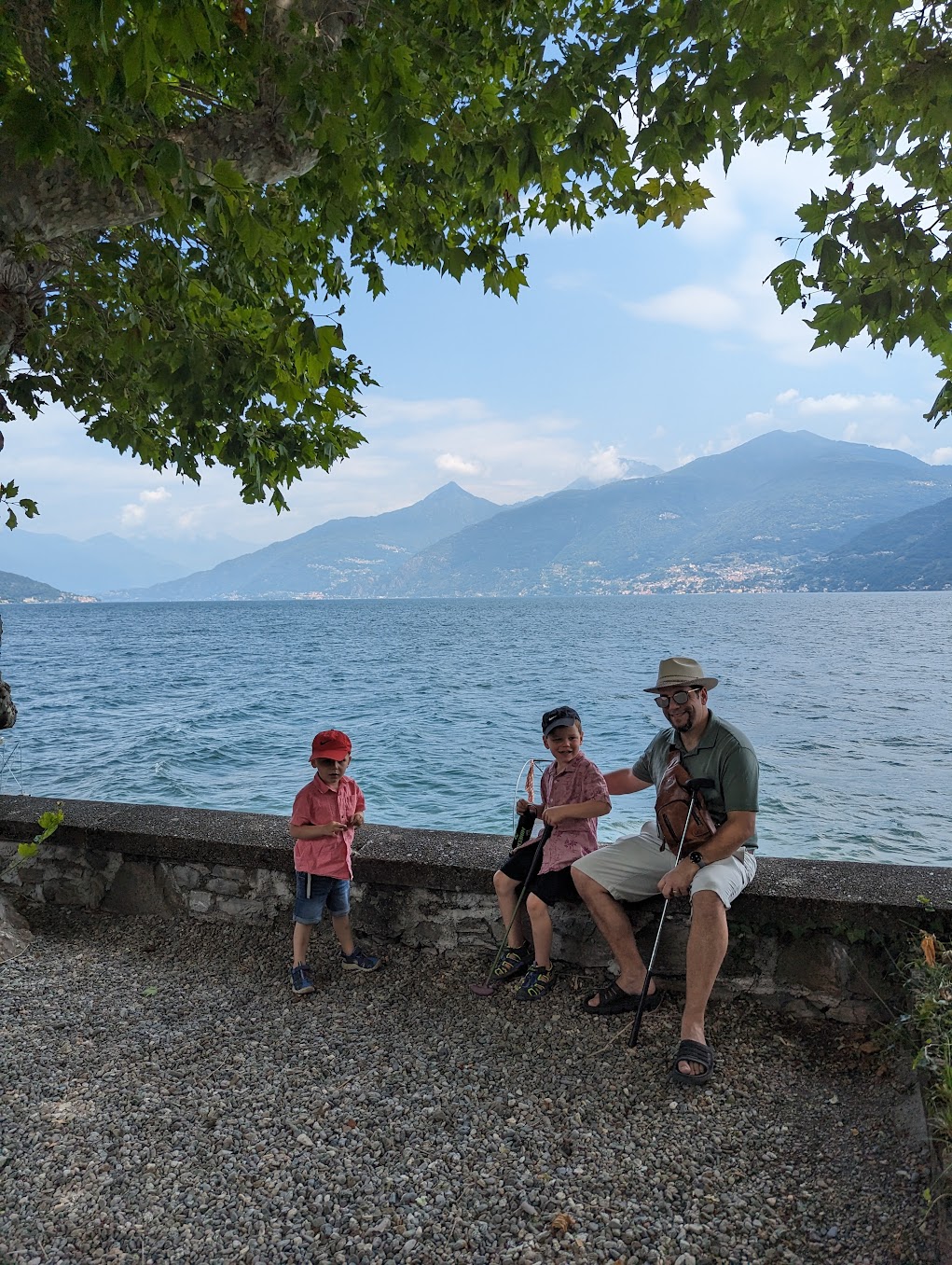 a man and two children sitting on a stone wall by a lake