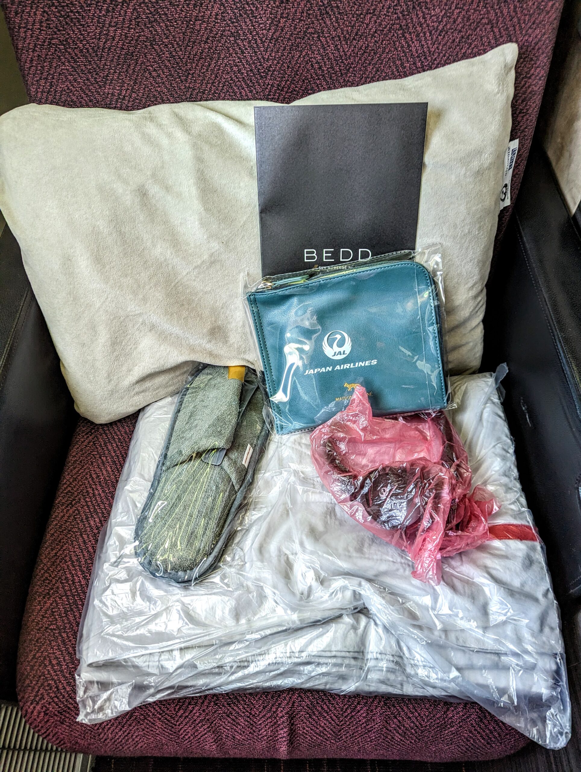 a bed with a bag of clothing and a blanket