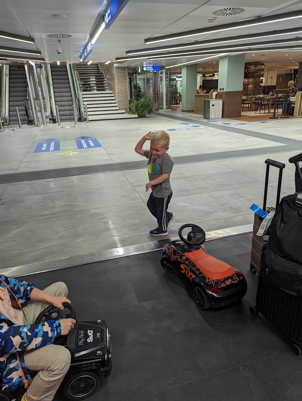 a boy standing in a large room with a toy car and a couple of people