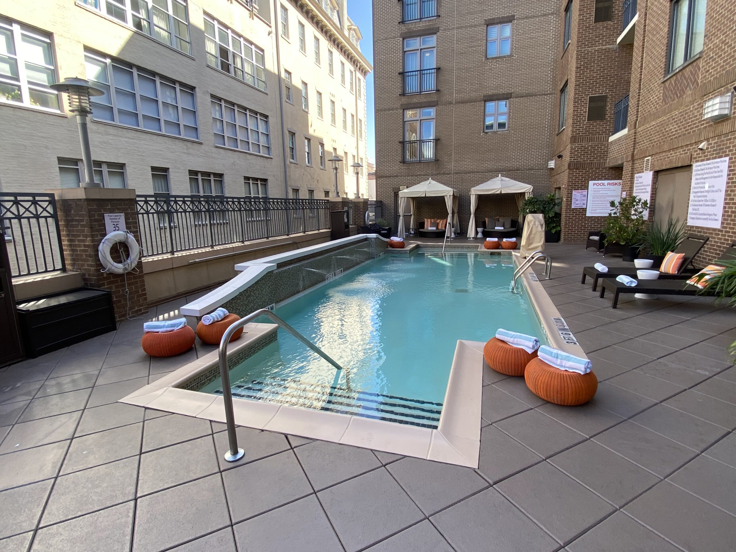 a pool with a railing and chairs in front of a building