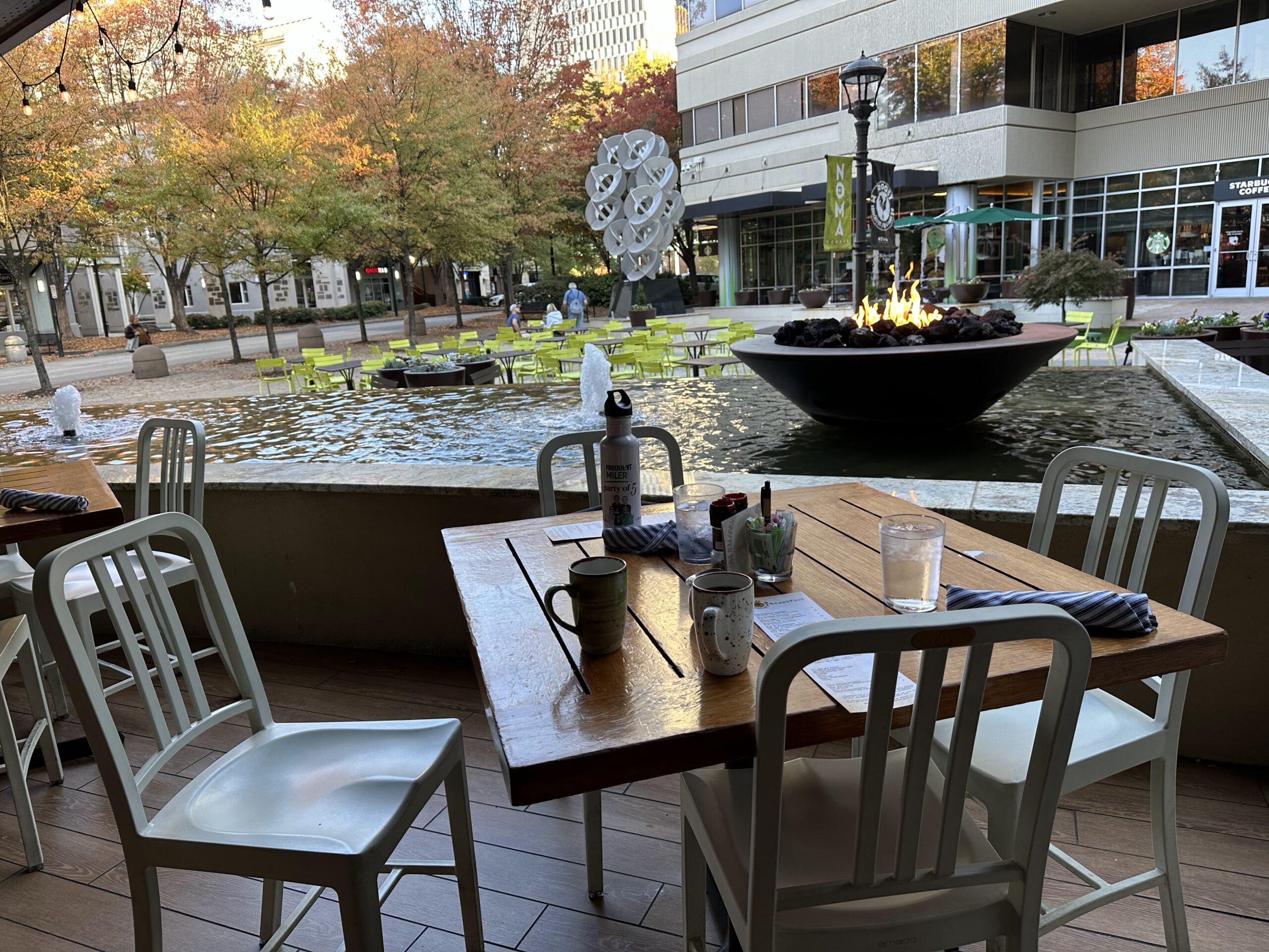 a table and chairs outside with a fountain in the background