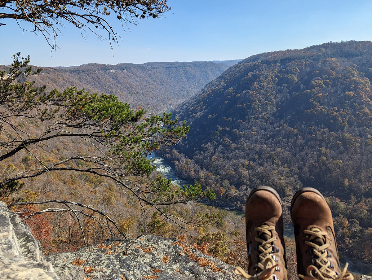 a person's legs on a cliff overlooking a valley