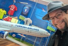 a man wearing a hat and glasses standing next to a model airplane
