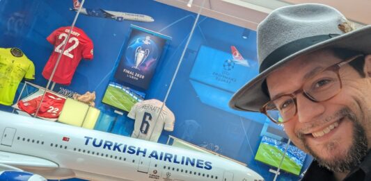 a man wearing a hat and glasses standing next to a model airplane