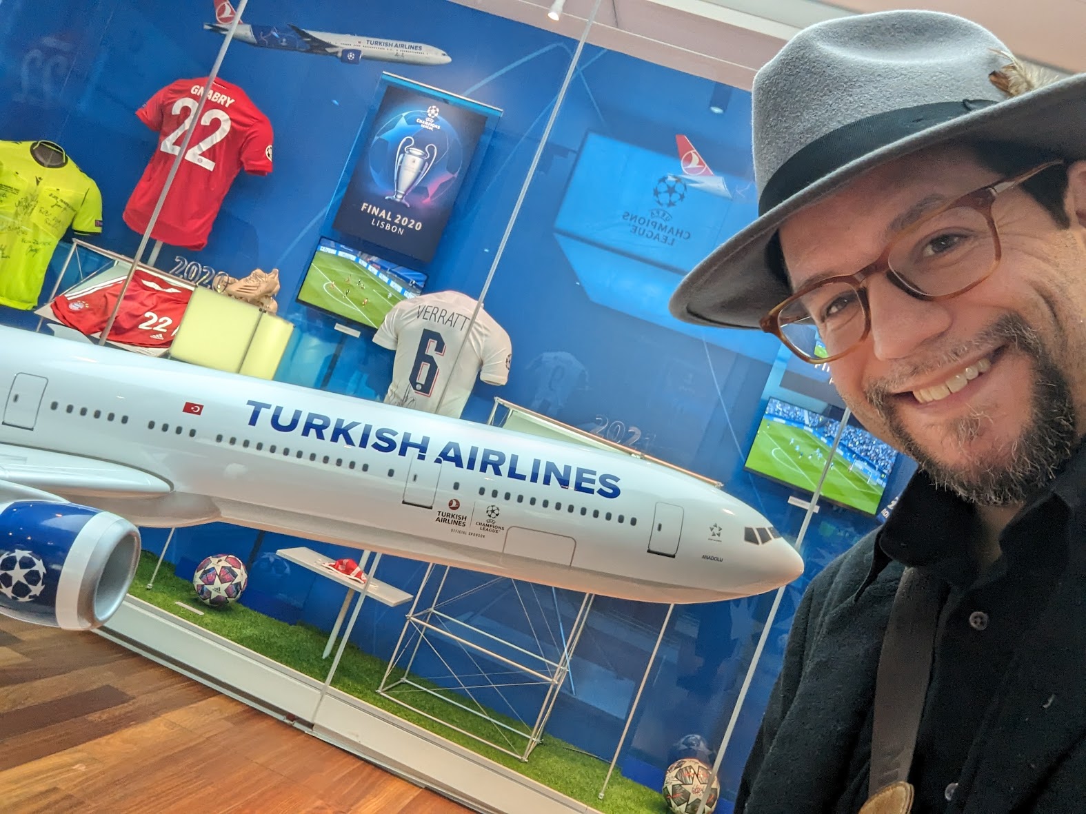 a man wearing a hat and glasses standing next to a model airplane