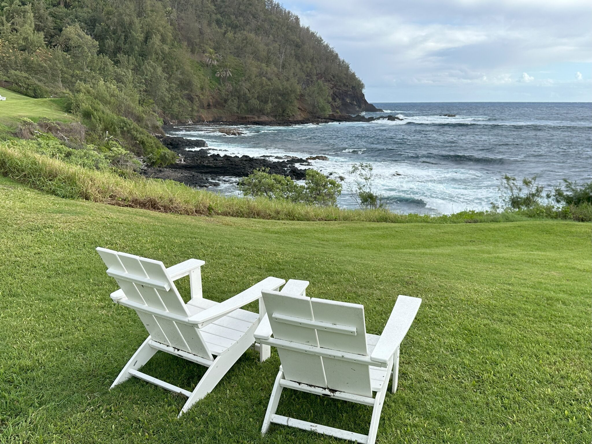 two white chairs on grass by the ocean