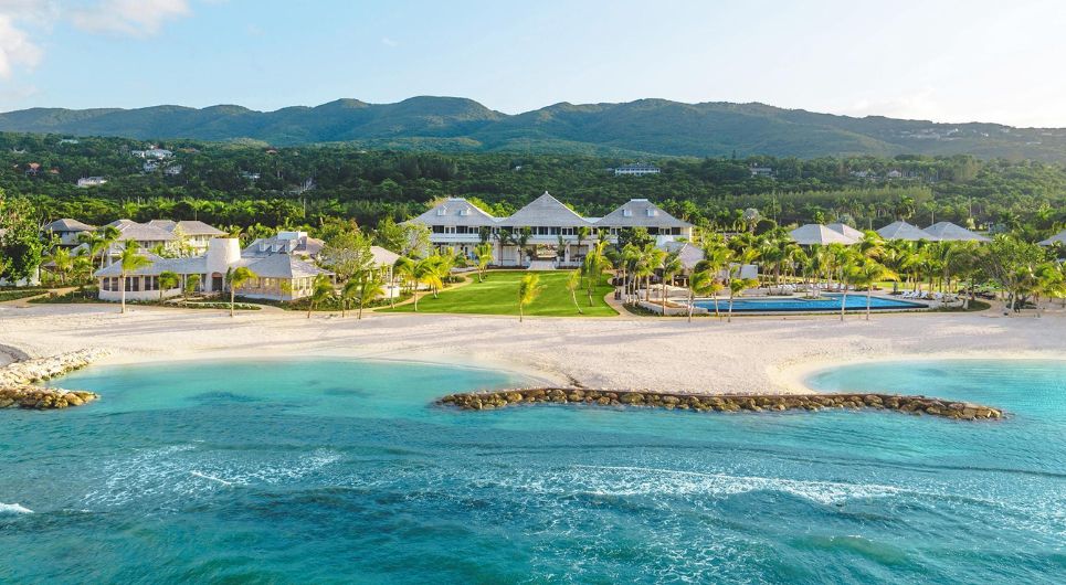 Luxury ocean-side resort hotel with green hills in the background and blue ocean in the foreground