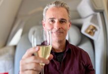 Greg in Emirates first class raising a champagne glass towards the viewer